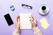 Woman hand with pencil writing on notebook and hold coffee cup. Woman working on office table with coffee