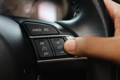 the driver's hand presses the cancel button to set the cruise control feature on modern cars.  cruise control button on the steering wheel of a luxury car
