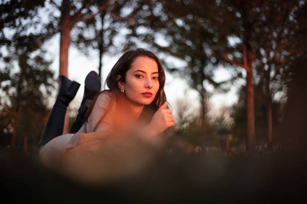 Brunette woman is lying on the grass in nature.She is wearing a casual clothes at sunset.