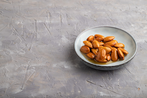 Almonds with honey on gray concrete background. side view, close up, copy space.