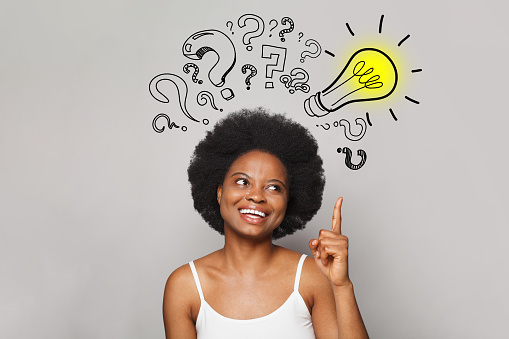 Smiling happy african american woman with idea pointing up to light bulb on grey background