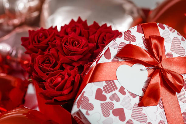 Valentine's day. Red roses in a white box in the form of a heart on the background of foil balls. A gift for women on a holiday. The concept of delivering flowers. floristry and flower shops. Valentine's Day holiday. A beautiful banner, a flyer for Valentine's day. Buying flowers for your beloved women. A concept for a flower shop. be my valentine stock pictures, royalty-free photos & images