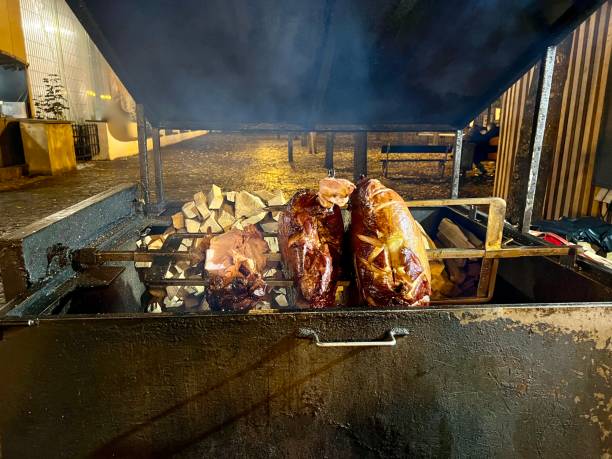 cottura della carne su una griglia allo spiedo, presa in un mercato all'aperto in europa. - spit roasted barbecue grill barbecue pork foto e immagini stock