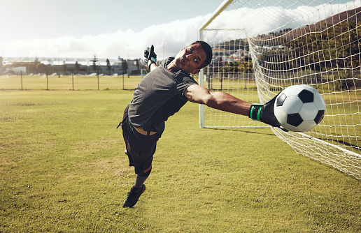 Soccer, sports and goalkeeper training on a field for a professional competition. Young and strong athlete with energy and motivation catching a football during a game or exercise on a sport ground
