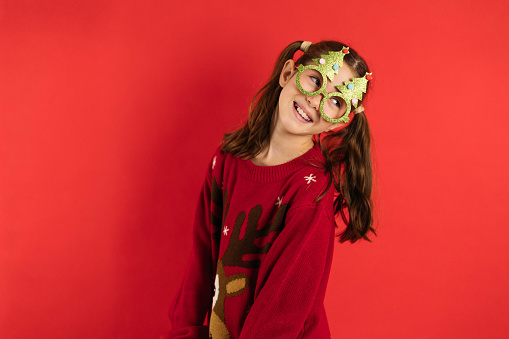 cute little girl with a cute facial expression posing in a Christmas sweater on a bright red background emotional Christmas concept.