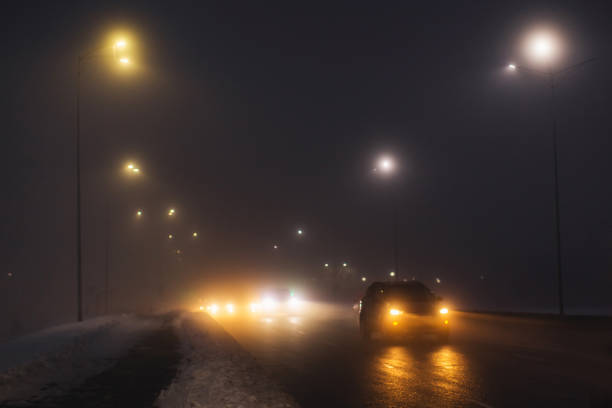 tempo nebuloso. neblina noturna. pouca visibilidade na estrada. movimento de carros. engarrafamento. asfalto escorregadio molhado. faróis de carro. raio de luz. neve e gelo na estrada. rua da cidade - traffic jam flash - fotografias e filmes do acervo