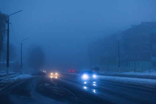 Foggy weather. Night fog. Poor visibility on road. Movement of cars. Traffic jam. Wet slippery asphalt. Car headlights. Ray of light. Snow and ice on road. City street