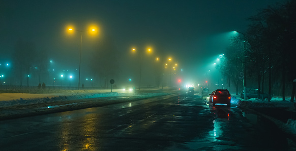 Foggy weather. Night fog. Poor visibility on road. Movement of cars. Traffic jam. Wet slippery asphalt. Car headlights. Ray of light. Snow and ice on road. City street