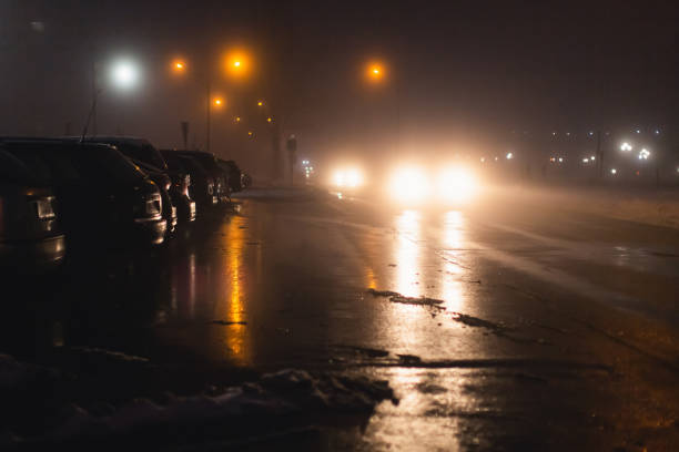 tempo nebuloso. neblina noturna. pouca visibilidade na estrada. movimento de carros. engarrafamento. asfalto escorregadio molhado. faróis de carro. raio de luz. neve e gelo na estrada. rua da cidade - traffic jam flash - fotografias e filmes do acervo