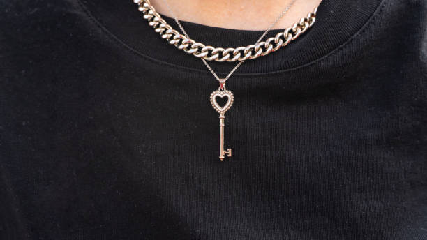 黒いジャケットの背景に対して、女の子の首の周りにキーの形のペンダントのクローズアップ。 - gold jewelry necklace locket ストックフォトと画像