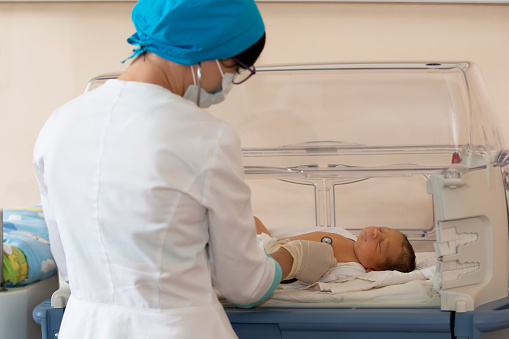 Neonatology. Doctor listening to the heartbeat of a newborn in an infant incubator