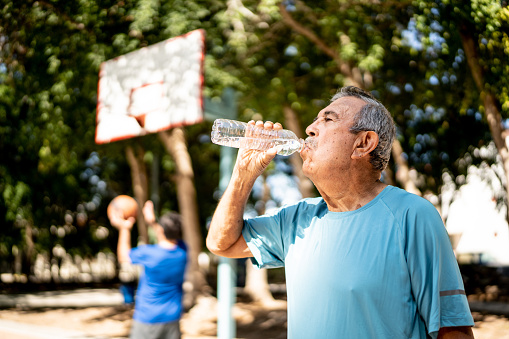 Senior man drinking water at the basketball court