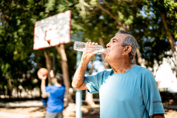 starszy mężczyzna pijący wodę na boisku do koszykówki - ciepła zdjęcia i obrazy z banku zdjęć