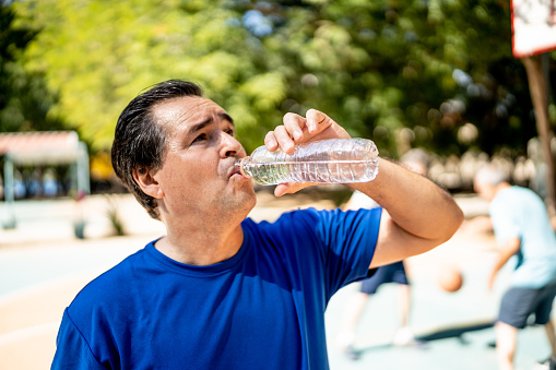 Portrait of a athletic man after doing exercises and holding a bottle of water, isolated over a white background