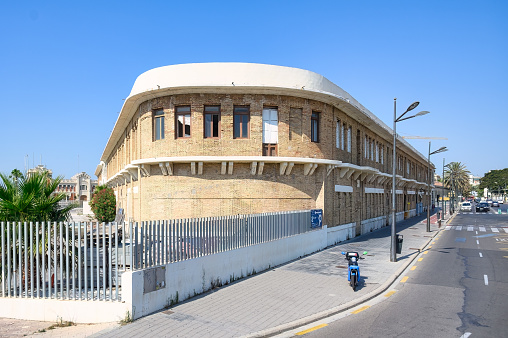 Valencia, Spain - July 16, 2022: A motorcycle parked on a sidewalk in a downtown area. Vehicles are on the street, and a large building is on one side of the road.