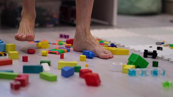 barefoot man walks among the scattered toys. Foot stepping on children's toys. Scattered toys on the floor. concept of an abundance of toys in the modern world