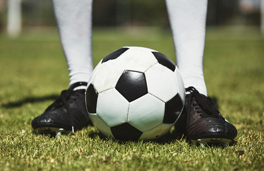 Soccer ball, football player and game of athlete on a sports field for a match wearing shoes. Fitness, training exercise and cardio health of male feet with energy on field, green grass or pitch