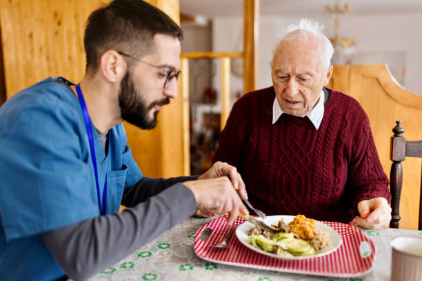 trabajador de cuidado masculino que sirve cenas a un hombre mayor en su casa - care community 80 plus years cheerful fotografías e imágenes de stock