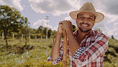 Portrait of young man in the casual shirt holding his hoe in the farm. Farm tool. Latin man.