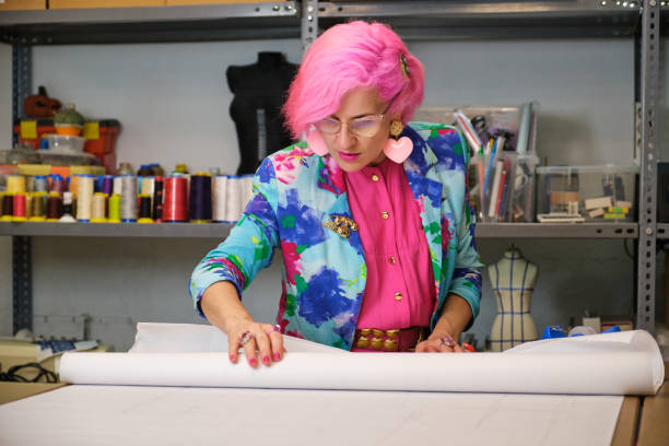 istock Seamstress with pink hair and colorfull clothes unrolling sewing patterns. 1444974335