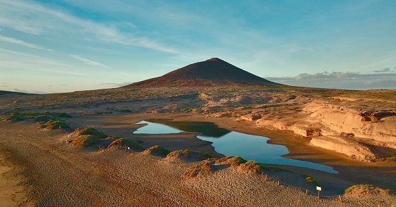 Aerial view of volcanic cone of Montaña Roja and sea lagoon during sunrise at El Medano, Tenerife Canary Islands