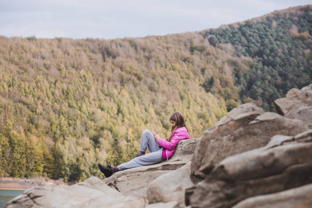 istock Young girl sitting on rocks using a smartphone and beautiful forest in background. Irati forest, Navarre, Spain. 1444976367