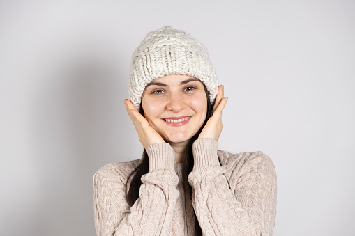A happy brunette woman in a winter hat and a knitted sweater smiles on a white background