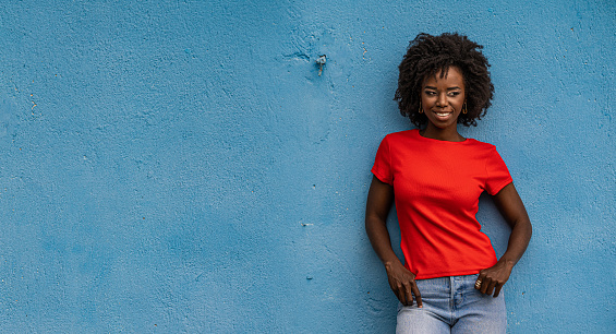 Attractive african young woman, wearing red t-shirt, posing against a blue background