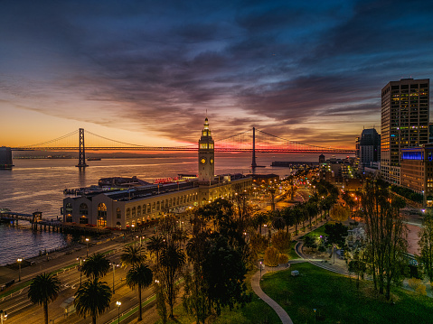 Aerial view of the Embarcadero with a burning sunrise and the Ferry Bldg. illuminated.