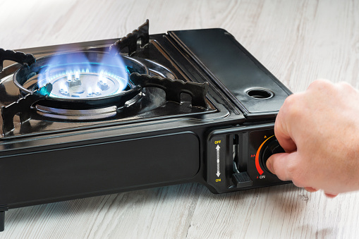 A man's hand turns on a portable gas stove on a wooden table. An alternative source for cooking at home during a power outage.
