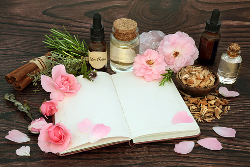 Aphrodisiac love potion preparation for Valentines Day. Magical spell recipe book or love letter with herbs, rose flowers, oil, spring water and rose quartz crystal. Wiccan occult concoction.