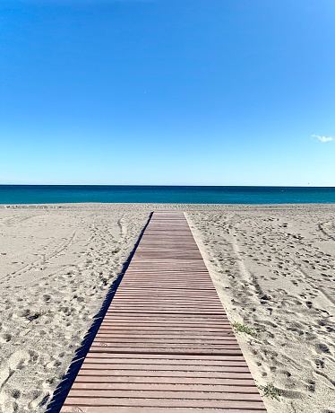 Wooden boardwalk on a sandy beach. Path leading to the beach with the sea in background.
