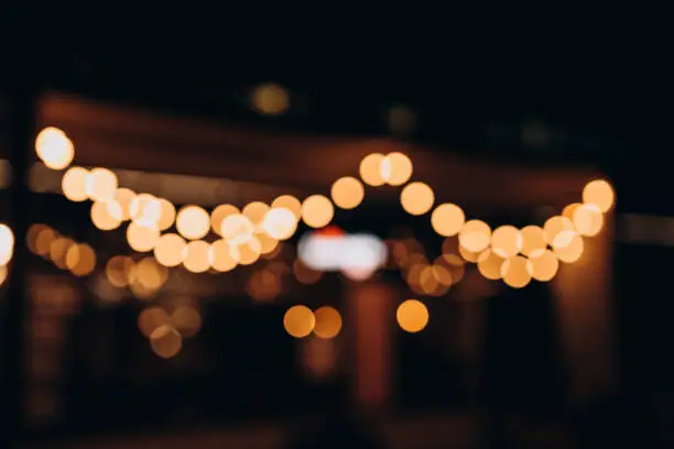 Photo of Decorative outdoor string lights at night time, Defocused Background, night city life backdrop, party time with Yellow bokeh balls