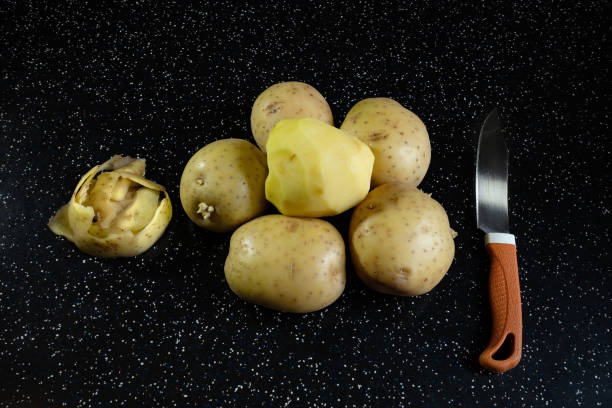 Potatoes on a black table and a knife close-up. Peeling fresh potatoes stock photo