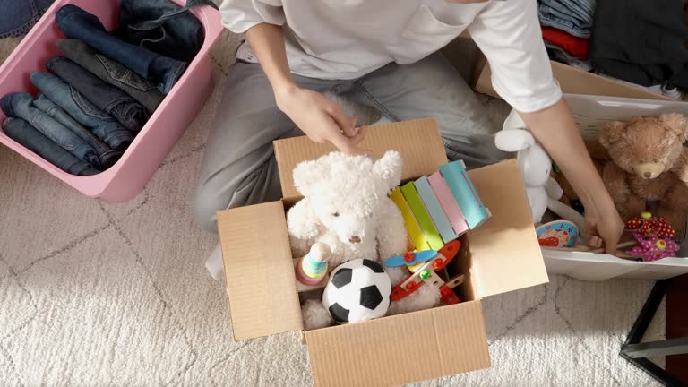 Boy preparing clothes and toys for charity donation. Teenage boy sorting and kid toys, clothes into boxes at home. Kid playing with old toys and packing them to cardboard box