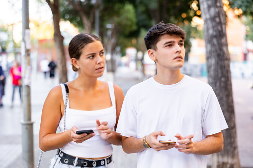 Modern young man and woman strolling together and phubbing