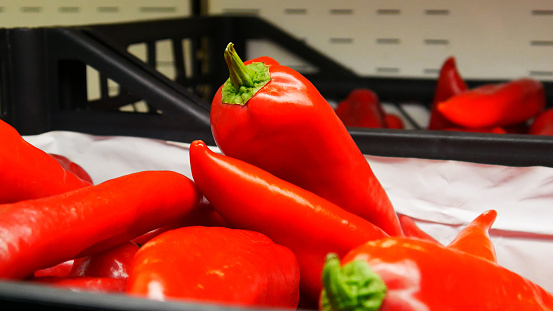 Many very beautiful ripe red peppers in a trading basket close-up