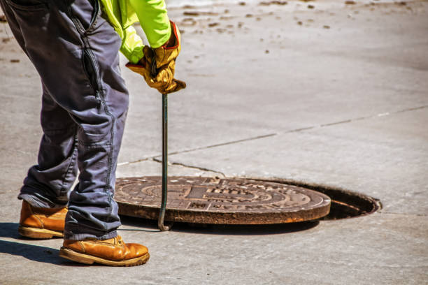 istock Man removing or replacing a heavy manhole cover in paved street with hook - selective focus and copy space 1444996780