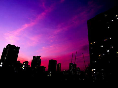 Silhouette of building, cityscape on purple and blue sky background. Lighting bokehs on business building on dark after sunset. Abstract night urban backgrounds.
