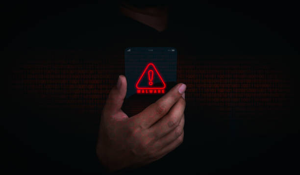 istock Malware concept. Red malware icon alert on futuristic transparent smart mobile phone in businessman hand on dark background. Detection of virus technology, system hack by hacker, crime, cyber attack. 1444996904