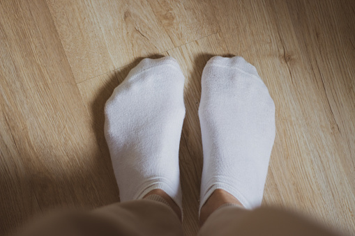 White socks on the floor. Women footwear. Warm clothing concept. Comfortable cotton clothes. Domestic life backgrounds. White socks on girls feet. Winter fashion. Legs in socks on laminate floor.