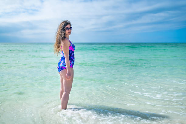 원피스 수영복을 입은 젊은 여성 여성이 플로리다주 플로리다주 시사이드의 청록색 물 낙원 안에 서 있다 팬핸들에 있는 멕시코만 해변 - 16707 뉴스 사진 이미지