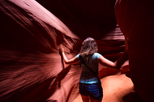 Young woman back inside Upper Antelope slot canyon, Arizona standing leaning touching sandstone rock formations between walls
