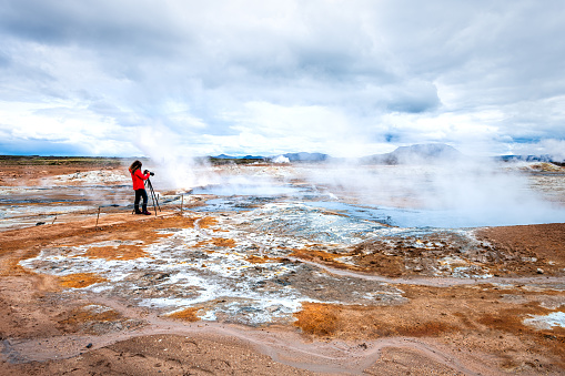 Hot steam bubbling boiling blue mud geyser and woman photographer in Hverir geothermal spot area in Iceland by Myvatn caldera lake
