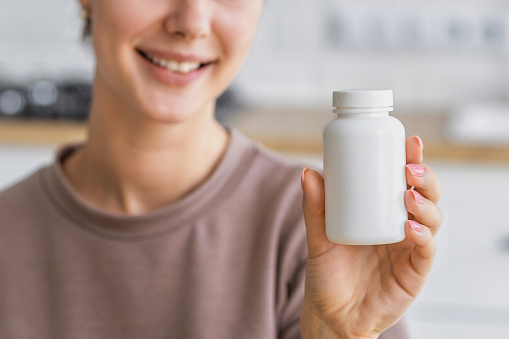 Happy young caucasian woman holding bottle of dietary supplements or vitamins in her hands. Close up. Healthy lifestyle concept