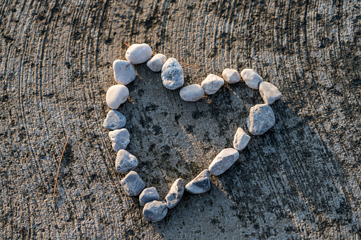 Small pebbles set together in a shape of heart on beach at sunset.