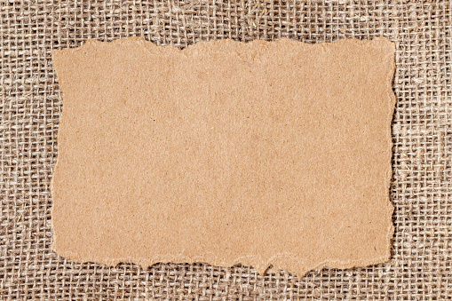 Torn scrap of craft paper on natural sacking burlap background, copy space