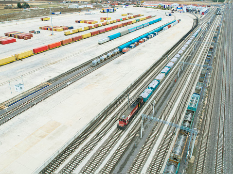 freight train carrying freight container, with rows of containers in the background, drone view