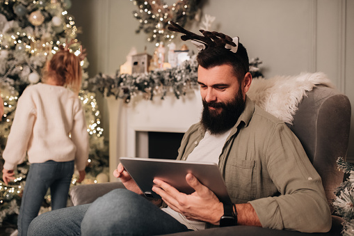 Loving family celebrating Christmas together indoors. Family of four exchanging gifts, playing around the Christmas tree in their living room, sitting next to a fireplace. Lovely couple celebrating New Years eve with their daughters. Father doing some last minute Christmas shopping online. Man working during the holidays on his digital tablet.