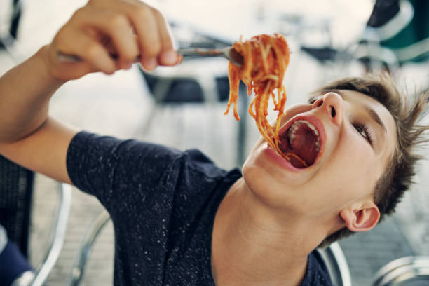 adolescent qui aime beaucoup manger des spaghettis. - child eating pasta spaghetti photos et images de collection